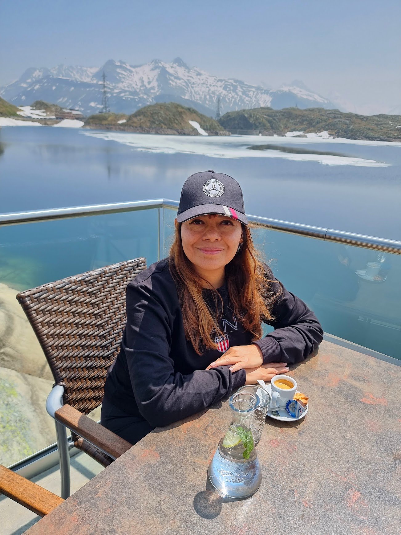 mujer vestida de netro con una gorra negra y de fondo un lago de agua turquesa con montañas con nieve